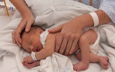 Baby liegt auf der Seite auf dem Schoß der Mutter im Krankenhausbett.