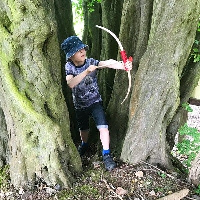 Minibogen aus Eschenholz und Sicherheitspfeile für drinnen und draußen Ein Kind im Wald mitPfeil und Bogen aus Holz