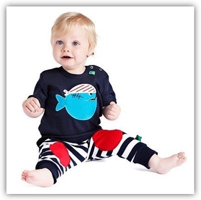 Mit Alltagskleidung kann man sich auch gut verkleiden Kind sitzt auf dem Boden und trägt ein T-Shirt mit einem Piraten-Fisch und eine blau-weiß-gestreifte Hose mit roten Aufnähern an den Knien
