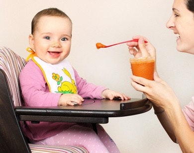 Mutter füttert ihr Baby, das in einem Stuhl sitzt, mit Brei Mutter füttert ihr Baby, das in einem Stuhl sitzt, mit Brei