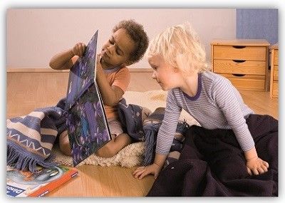 2 Kinder schauen sich, eingekuschelt in Decken, ein Buch an