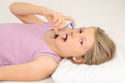 Mädchen liegt im Bett und nimmt einen Zug aus einem Inhalator
