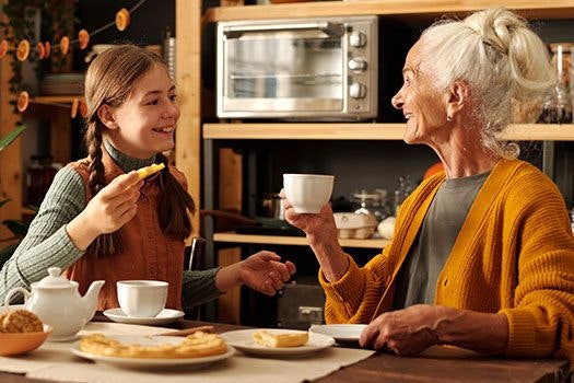 Oma und Enkelin sitzen bei Kuchen zusammen und reden.