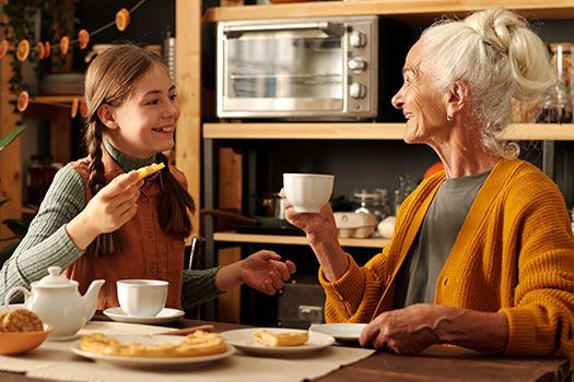 Oma und Enkelin sitzen bei Kuchen zusammen und reden.