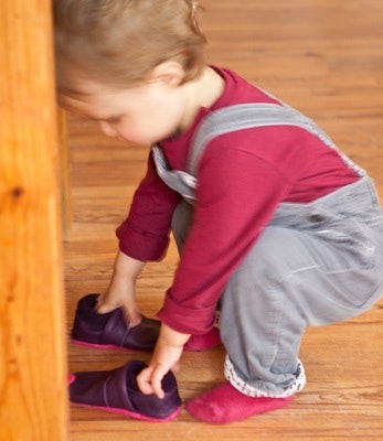 Lieblinge Krabbelschuhe Ein kleines Kind, welches nach Leder-Krabbelschuhen greift, die vor ihm liegen.