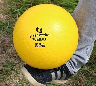 Ein gelber Greenstories Schaumstoff-Fußball, auf dem Fuß eines Kindes