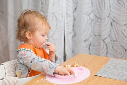 Baby sitzt im Babystuhl am Tisch und isst von seinem Teller
