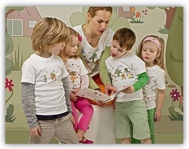 Frau liest 4 Kindern aus einem Patu-Buch vor, alle tragen Patu-T-Shirts Frau liest 4 Kindern aus einem Patu-Buch vor, alle tragen Patu-T-Shirts