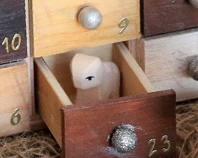Adventskalender befüllen mit Krippenfiguren aus Holz Adventskalender aus Holz mit Schubladen. Eine Schublade ist geöffnet, es steht ein Lamm aus Holz drin