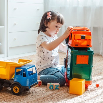 Mädchen, dass auf dem Boden sitzt und mit Spielzeug-LKW spielt.