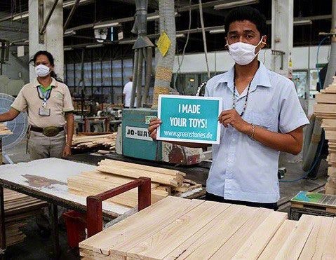 Arbeiter in der PlanToys Fabrik Arbeiter in der Fabrik von PlanToys in Thailand hält ein Schild hoch mit der Aufschrift "I made your toys°!.