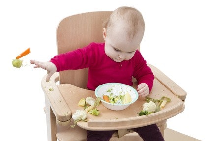 Baby sitzt in einem Hochstuhl und wirft mit Brokkoli, Möhren, Blumenkohl und Kartoffeln, die in der Schale vor ihm waren Baby sitzt in einem Hochstuhl und wirft mit Brokkoli, Möhren, Blumenkohl und Kartoffeln, die in der Schale vor ihm waren