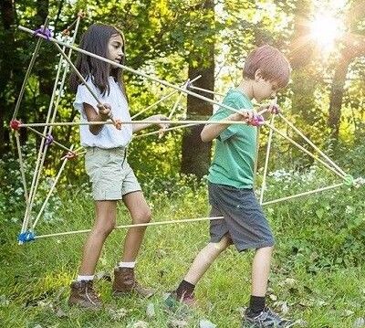 zwei Kinder im Wald tragen eine Konstruktion aus Stöcken und Stick-lets. Es könnte eine Rakete sein, in der die Kinder drin sind,