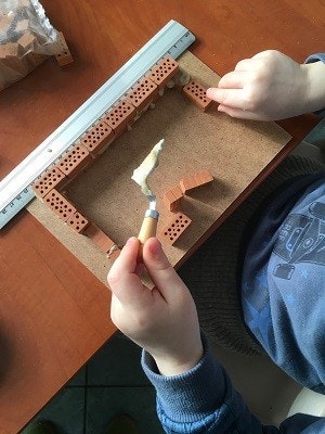 Steinbaukasten teifoc Man sieht die Hände eines Kindes von oben, wie es aus kleinen Steinen und einer kleinen Kelle voll Mörtel eine Wand baut