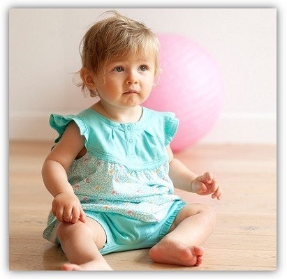 Kindermode People wear organic Ein Kleinkind sitzt auf dem Boden, es hat einen Strampler an.