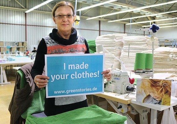 Mitarbeiterin bei disana disana-Mitarbeiterin hält ein Schild mit der Aufschrift "I made your clothes!" hoch.