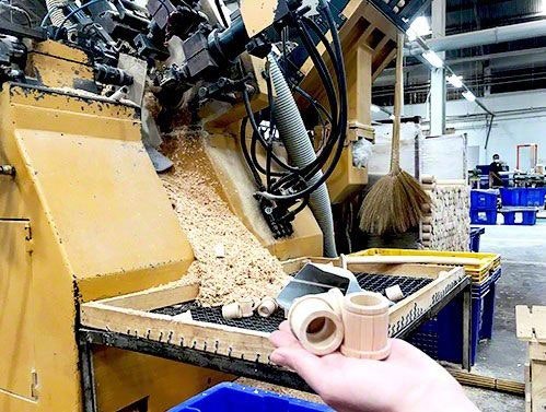 Neues Spielzeug aus Sägespänen Eine große Maschine, die Sägespäne zusammenpresst. Davor wird neues Spielzeug auf einer Hand gehalten.