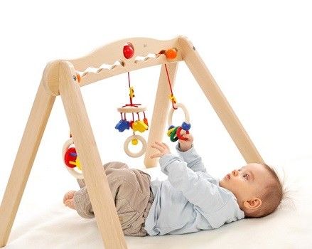 Baby liegt auf dem Rücken unter dem Spielbogen und greift nach den Greiflingen