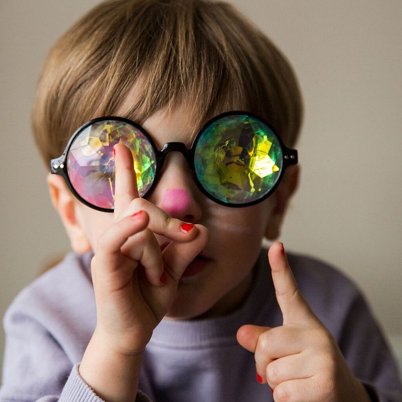Junge mit bunter Brille, eine rosa geschminkte Nase und roten Nagellack