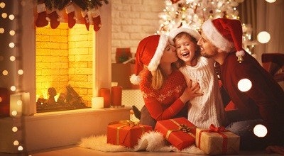 Mutter, Vater und Tochter sitzen eng beieinander vorm Kamin in einem weihnachtlich dekorierten Zimmer. Vor ihnen liegen Geschenke. Mutter, Vater und Tochter sitzen eng beieinander vorm Kamin in einem weihnachtlich dekorierten Zimmer. Vor ihnen liegen Geschenke.