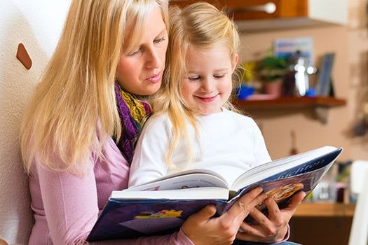 Mutter liest ihrer Tochter auf ihrem Schoß etwas vor.