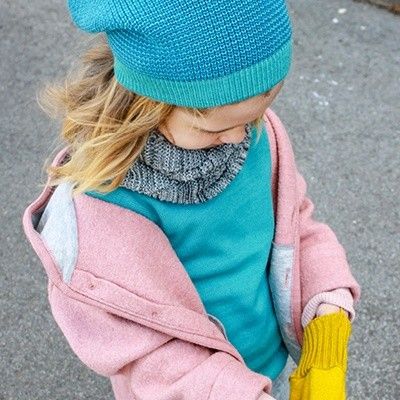 Ein Kind auf einer Straße, mit Disana-Mütze, Mantel, Schal, Handschuhe und Pullover.