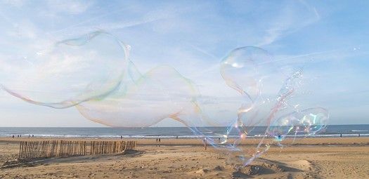 Riesenseifenblasen, die über den Strang schweben, im Hintergrund das Meer.