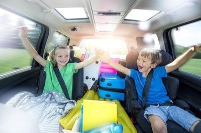 Das Auto ist voll, ein Mädchen und ein Junge sitzen auf der Rückbank und freuen sich auf den Urlaub.