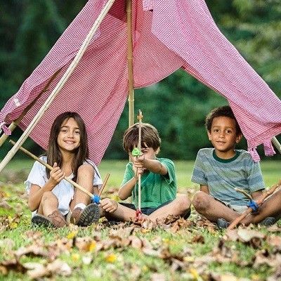 Drei Kinder in der Natur unter einem selbst gebauten Zelt. Sie haben Schwerter und Pfeil und Bogen in den Händen