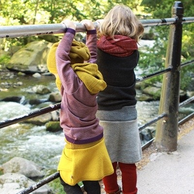 Disana Outfits in verschiedenen Größen erhältlich Zwei unterschiedliche große Kinder stehen draußen an einer Brücke, beide haben Disana-Klamotten an.
