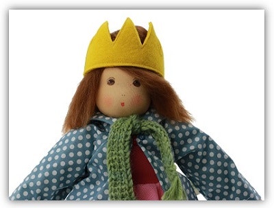 Stoffpuppe mit Haaren und Klamotten. Man sieht den Kopf und Oberkörper einer Stoffpuppe. Sie hat ein aufgemaltes Gesicht, Haare aus Wolle, eine Krone auf dem Kopf, eine Jacke und einen Schal an.