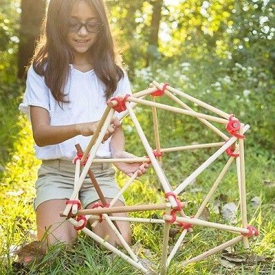 Ein Kind im Wald mit einer geometrischen Figur aus Stäben und Stick-lets gebaut.