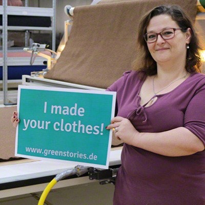 Gute Arbeitsbedingungen und zufriedene Mitarbeitende bei disana disana-Mitarbeiterin hält Schild mit der Aufschrift "I made your clothes!" hoch
