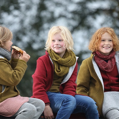 Drei Kinder sitzen draußen und tragen Wollkleidung von Disana. Drei Kinder sitzen draußen und tragen Wollkleidung von Disana.