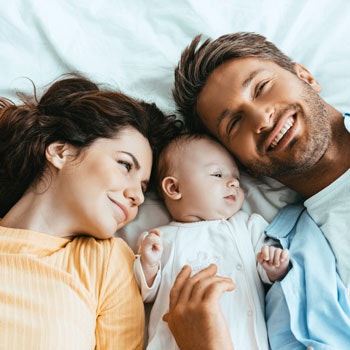 Mama und Papa liegen mit ihrem Baby auf einem Bett.