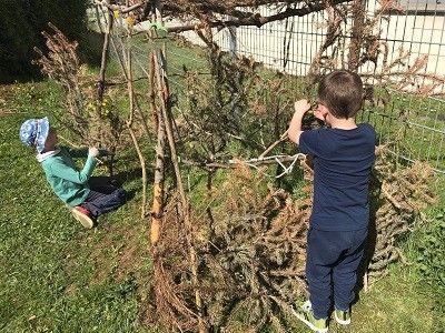 Zwei Kinder bauen im Garten ein Haus aus Stöcken