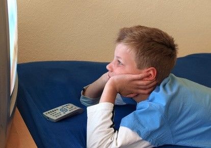 Junge liegt sehr dicht vorm Fernseher und schaut etwas.