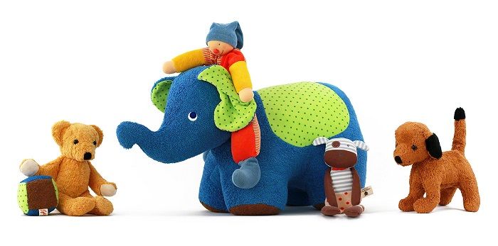 Eine Sammlung an Kuscheltieren: ein Teddybär, ein Elefant, eine Stoffpuppe, eine Kuh, ein Hund, ein Spielball aus Stoff.