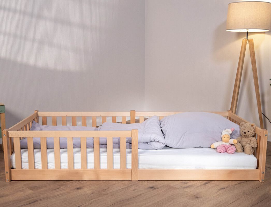 Ein Bodenbett in Naturholz mit einer Puppe und einem Teddy drin.