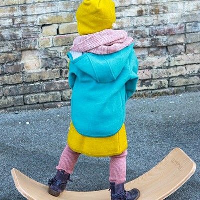 Ein Kind draußen auf einem Wobble Board. Es trägt einen Walkmantel in türkis.