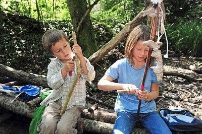 Junge und Mädchen sitzen im Wald auf Baumstämmen und schnitzen